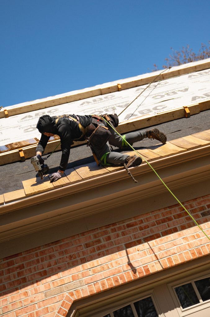Roofer installing cedar shakes with fall protection