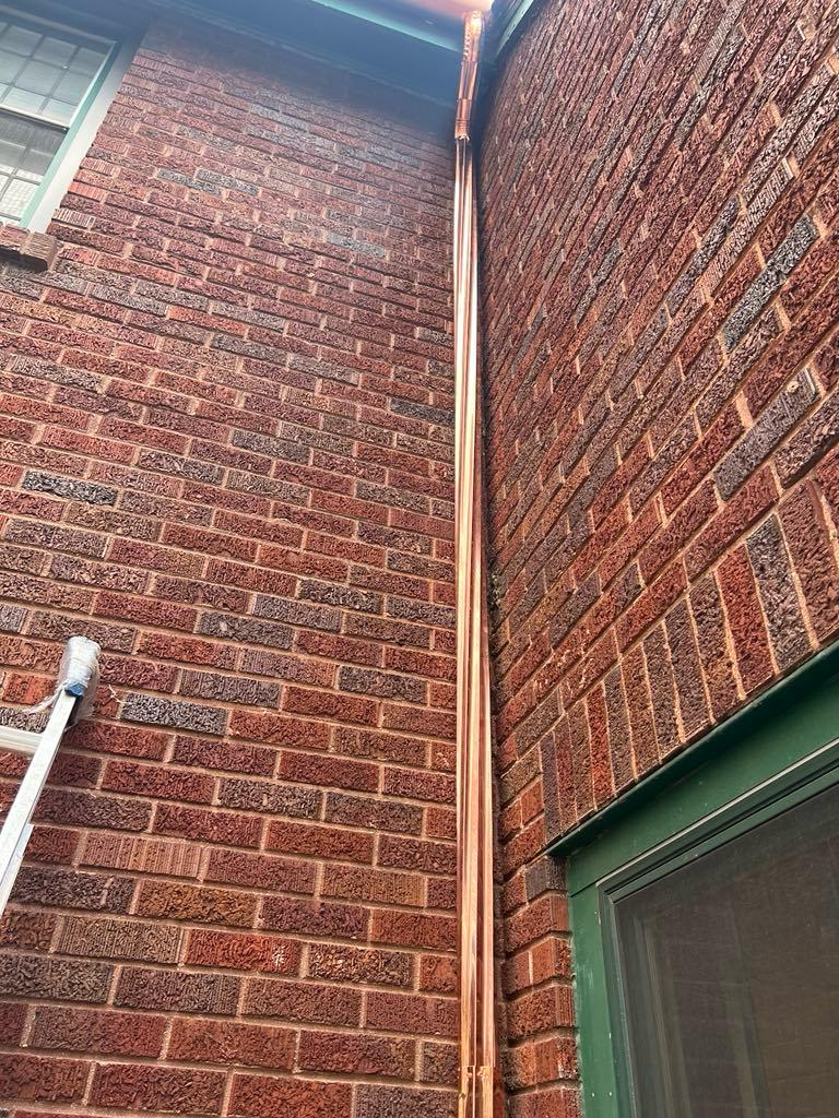 Copper downspout running down brick chimney